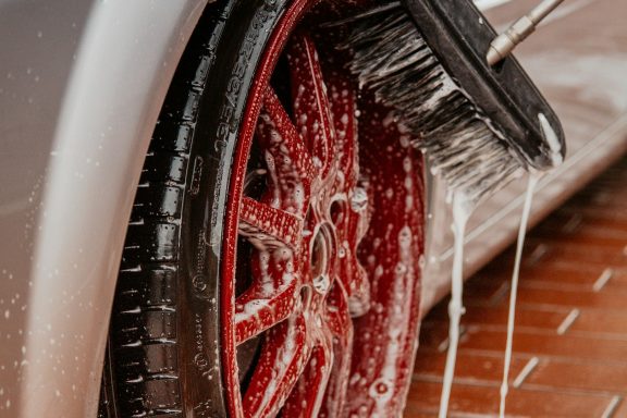 A close-up of a red wheel being cleaned with water and soap suds.